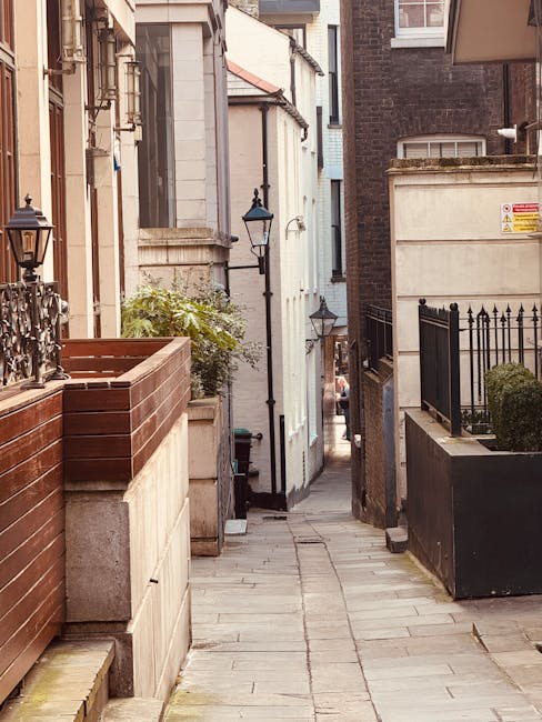 A row of multi-story residential buildings constructed from yellowish-brown brick with white window frames and arched window openings along a narrow street. The buildings have small front yards enclos